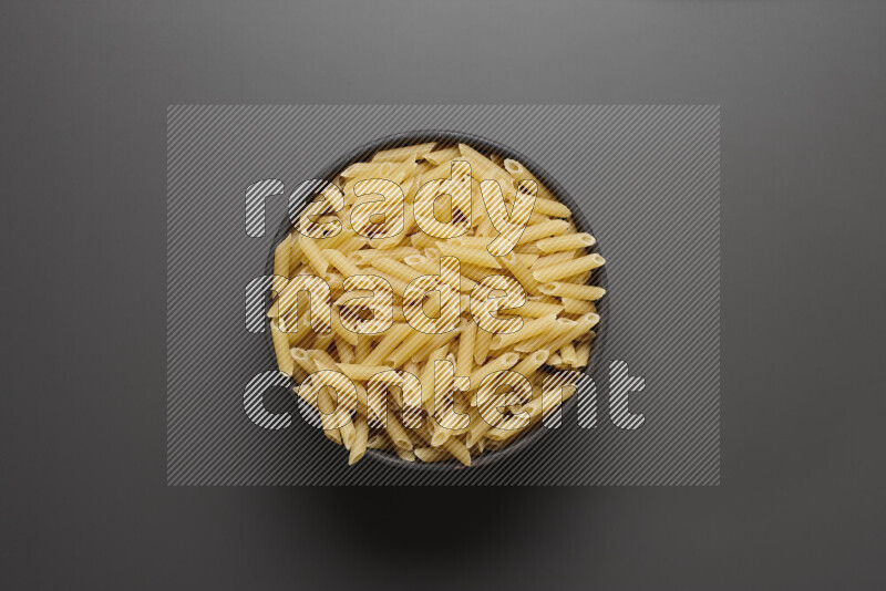 Mini penne pasta in a pottery bowl on grey background