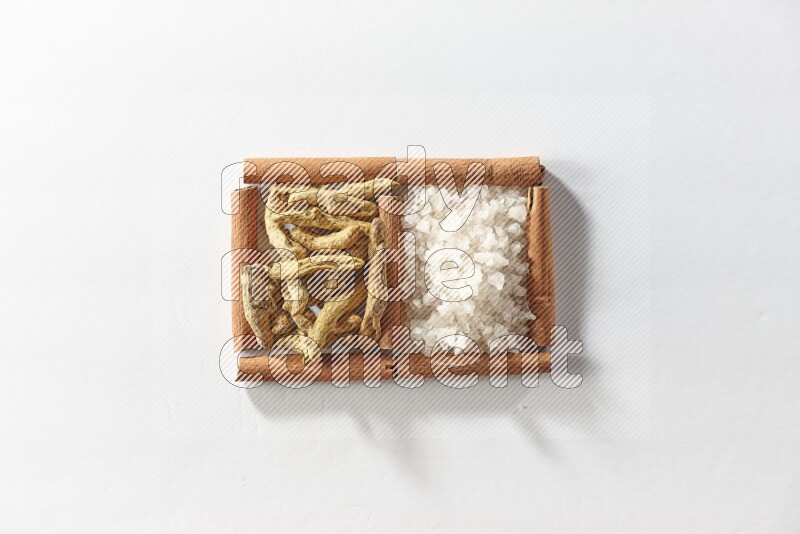 مربعان من أعواد القرفة ممتلئان بأصابع الكركم والملح الأبيض علي خلفية بيضاء