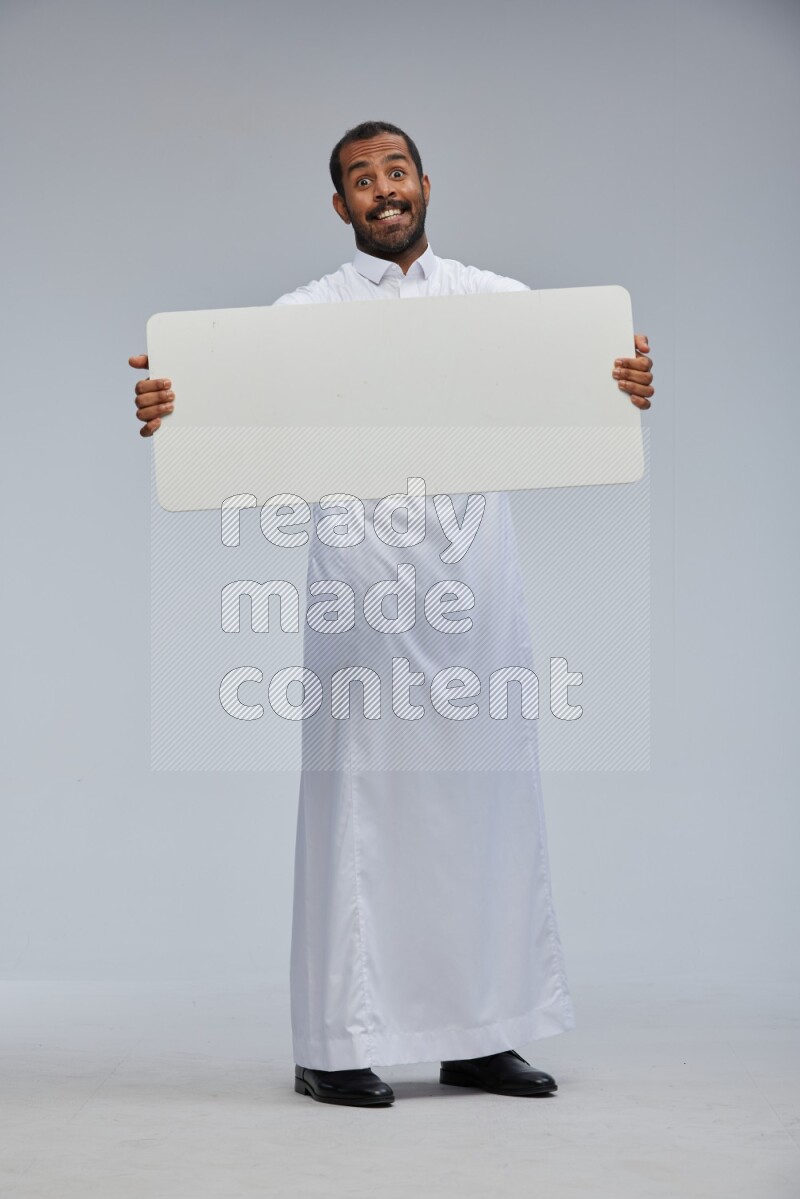 Saudi man wearing Thob standing holding board on Gray background