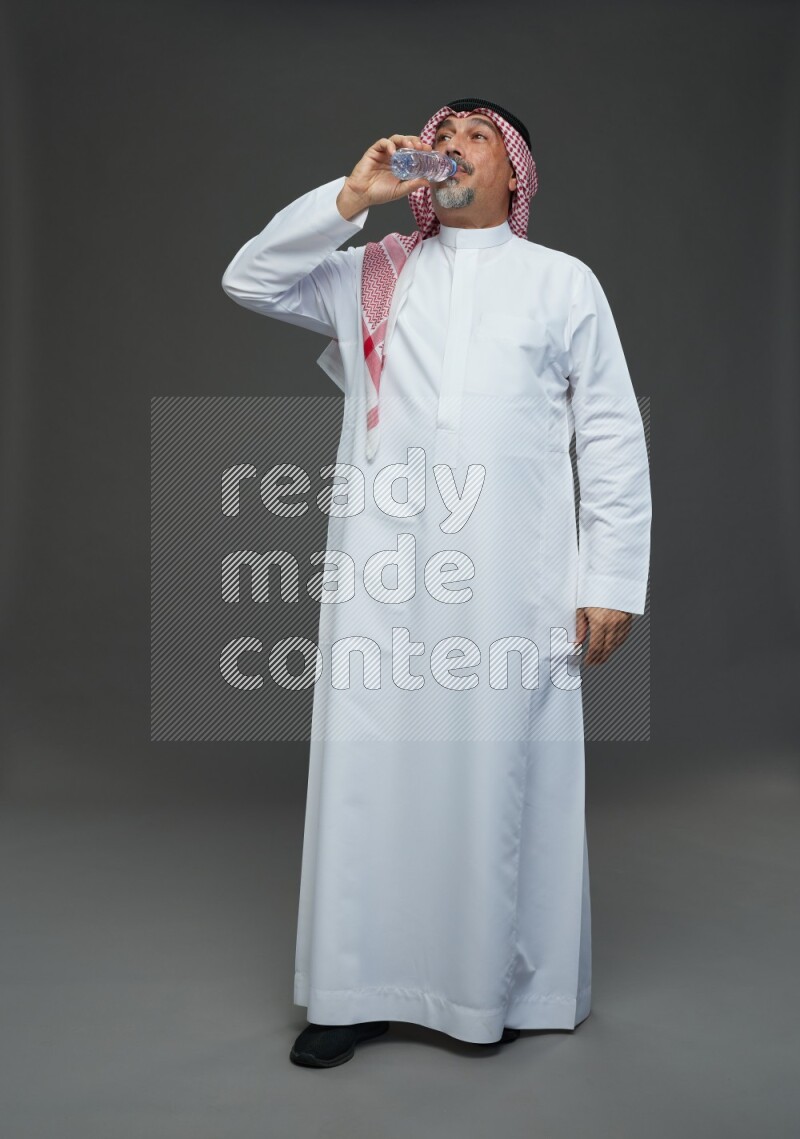 Saudi man with shomag Standing drinking water on gray background