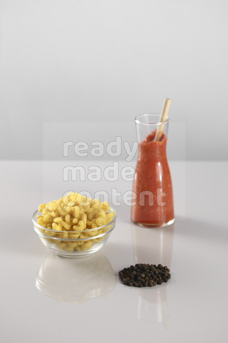 Raw pasta with tomatoe pasta with different ingredients such as cherry tomatoes, basil, garlic, bay laurel, cardamom, white pepper, black pepper, red chilis and wheat stalks on light grey background