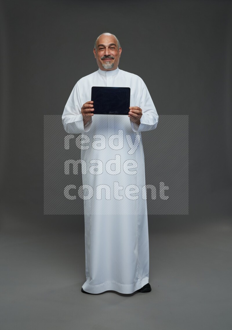 Saudi man without shomag Standing working on tablet on gray background