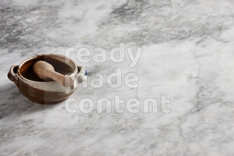 Multicolored pottery bowl with wooden honey dipper in it on grey marble background