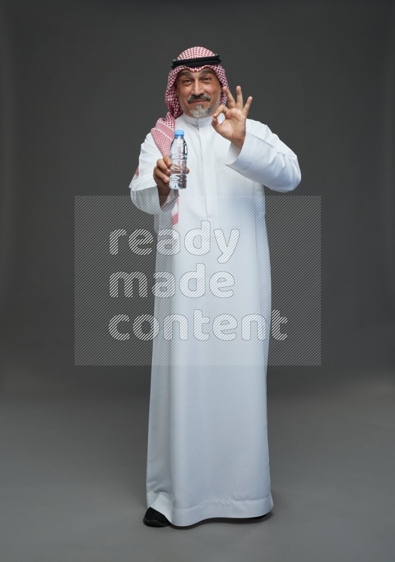 Saudi man with shomag Standing drinking water on gray background