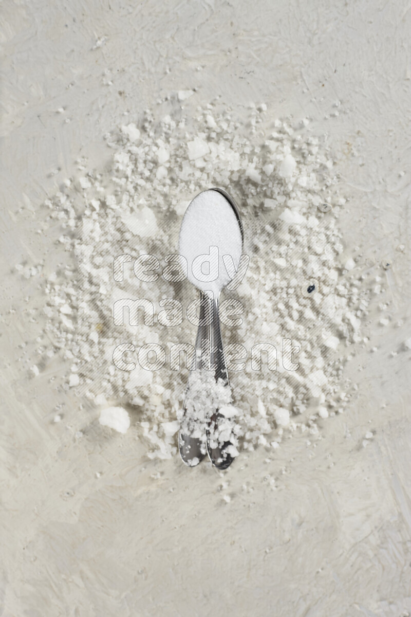 2 metal spoons filled with fine table salt and fine pink himalayan salt on white background