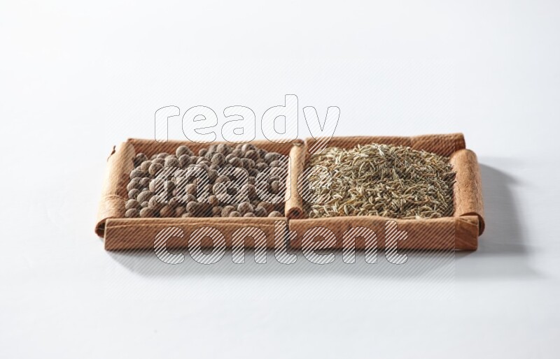 مربعان من أعواد القرفة ممتلئان ببهار الفلفل الحلو والكمون علي خلفية بيضاء