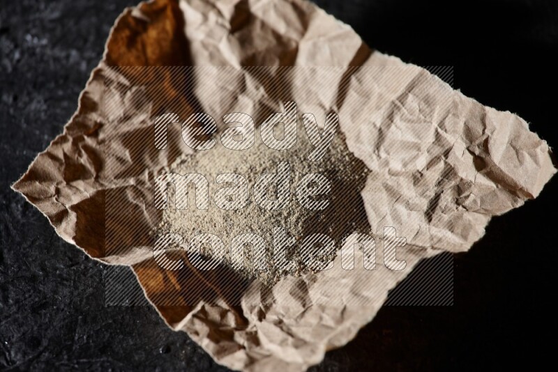 White pepper powder in a crumpled paper on textured black flooring