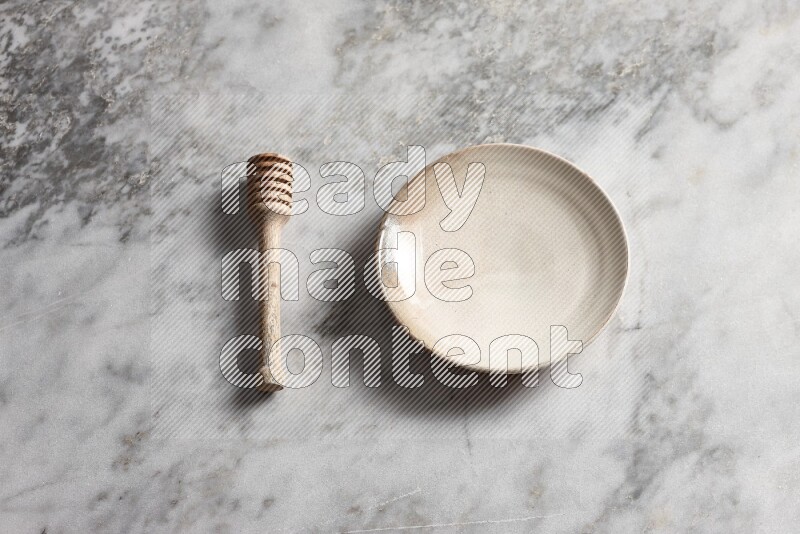 Beige pottery plate with wooden honey dipper on the side on grey marble background