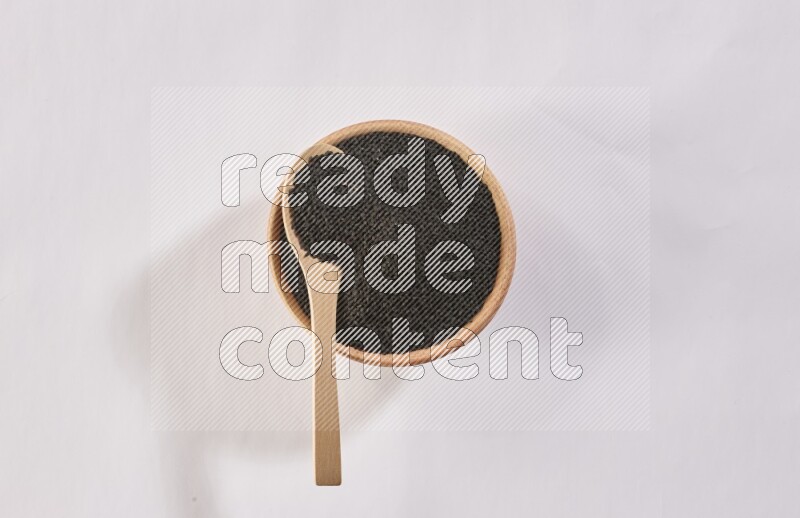 A wooden bowl and wooden spoon full of black seeds on a white flooring