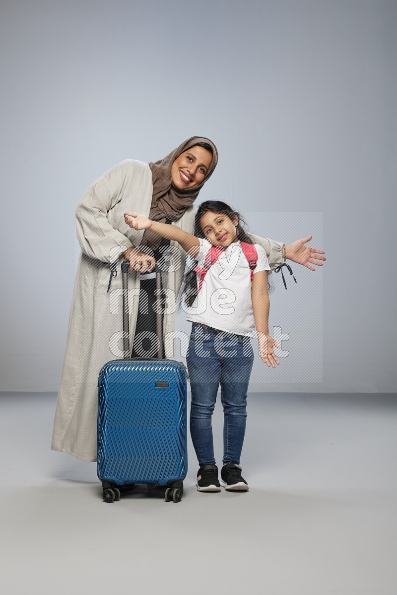 Mom and daughter standing pulling a carry-on bag on gray background