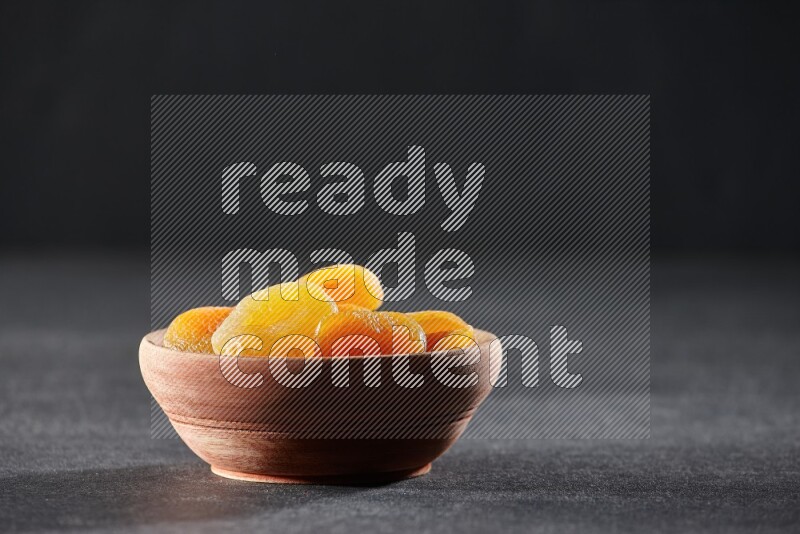 A wooden bowl full of dried apricots on a black background in different angles