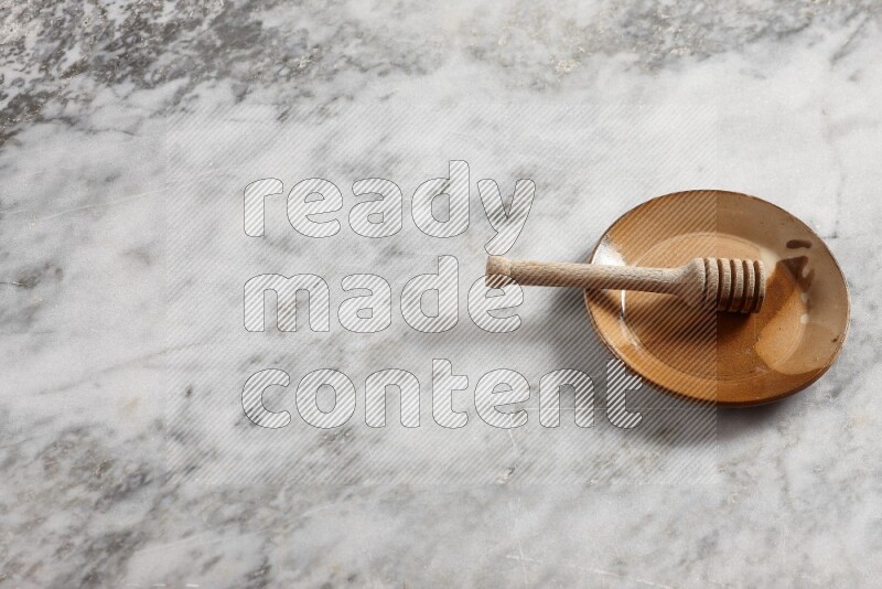 Multicolored pottery plate with wooden honey dipper in it on grey marble background
