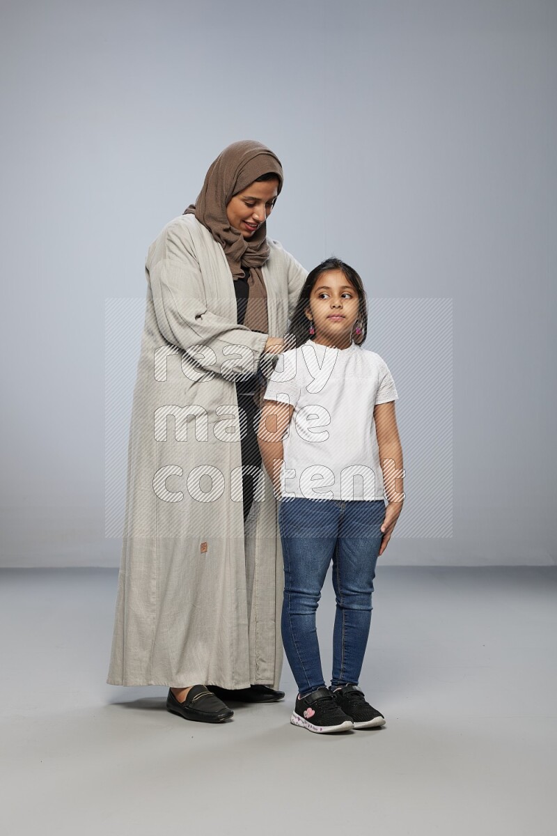 Mom standing styling hair for her daughter on gray background