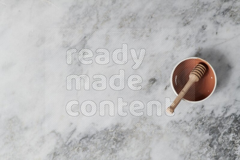Multicolored pottery bowl with wooden honey dipper in it on grey marble background