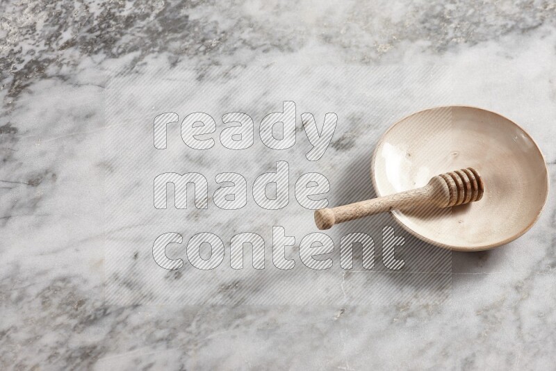Beige pottery plate with wooden honey dipper in it on grey marble background