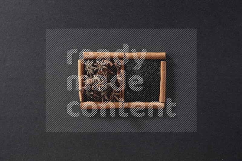 مربعان من أعواد القرفة ممتلئان بحبة البركة السوداء واليانسون النجمي علي خلفية سوداء