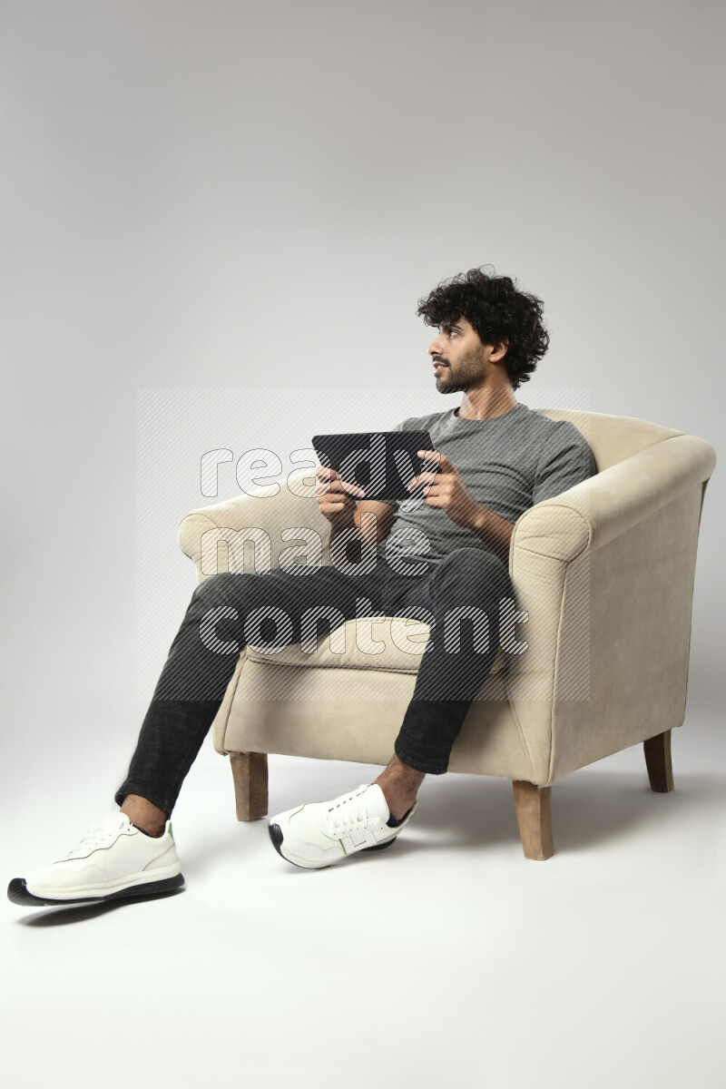 A man wearing casual sitting on a chair gaming on a tablet on white background