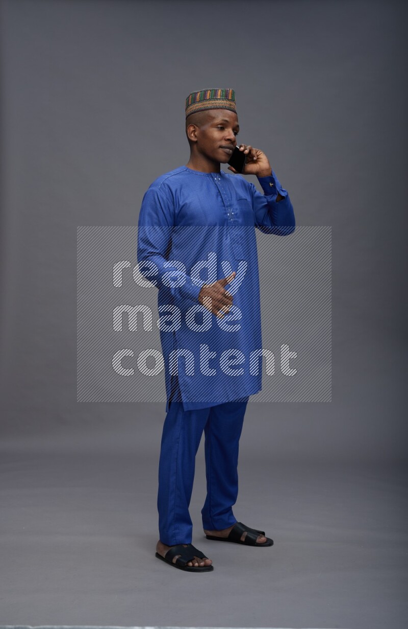 Man wearing Nigerian outfit standing talking on phone on gray background
