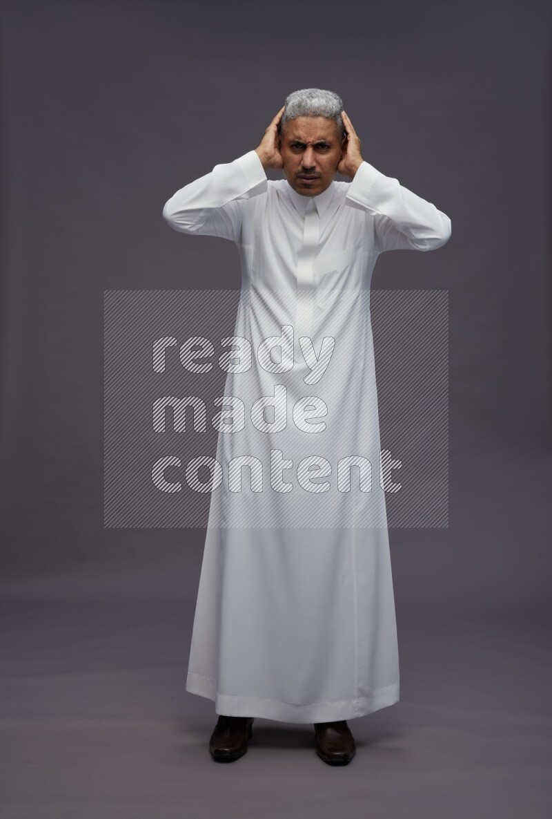 Saudi man wearing thob standing hands behind head on gray background