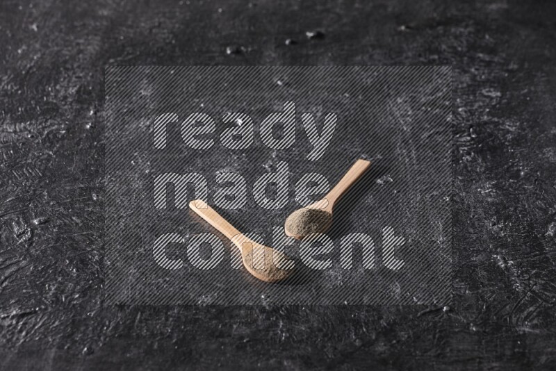 بودرة الفلفل الأسود في ملعقتان خشبيتان علي خلفية سوداء