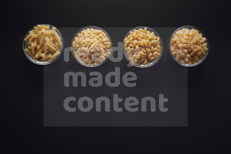 Different pasta types in glass bowls on black background