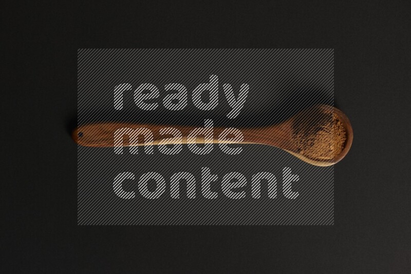 Cinnamon powder in a spoon ladle on black background