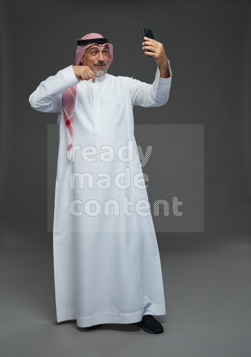 Saudi man with shomag Standing taking selfie on gray background