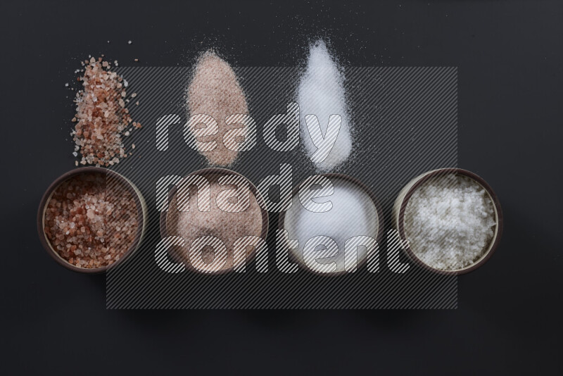 4 pottery bowls filled with himalayan salt and white salt on black background