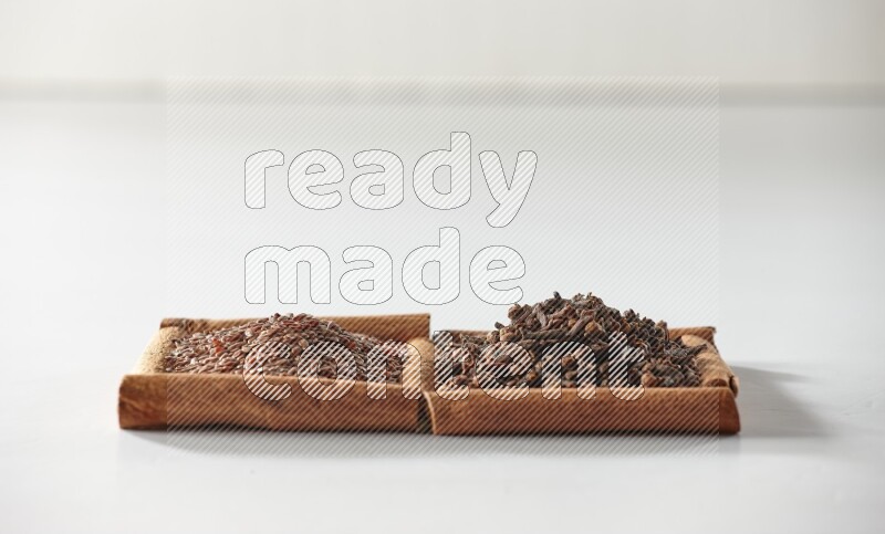 مربعان من أعواد القرفة ممتلئان بالقرنفل وبذور الكتان علي خلفية بيضاء