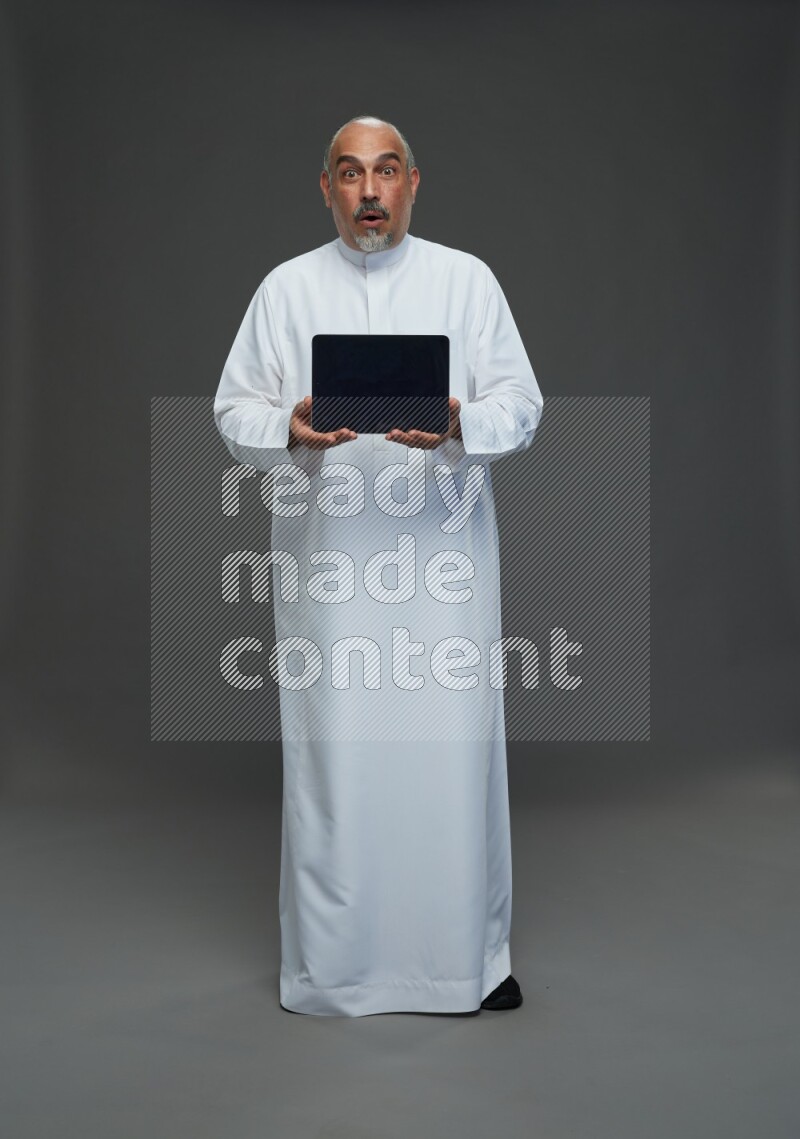 Saudi man without shomag Standing working on tablet on gray background