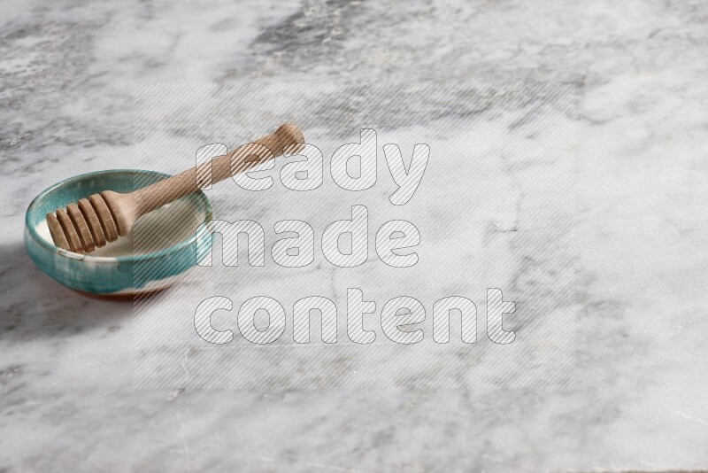 Multicolored pottery bowl with wooden honey dipper in it on grey marble background