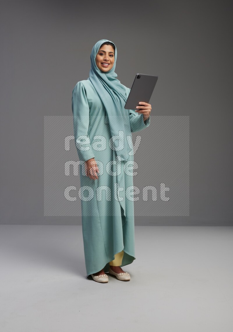 Saudi Woman wearing Abaya standing working on tablet on Gray background
