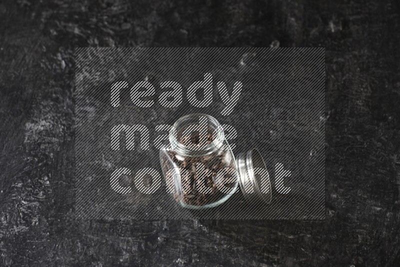 A glass spice jar full of cloves on textured black flooring