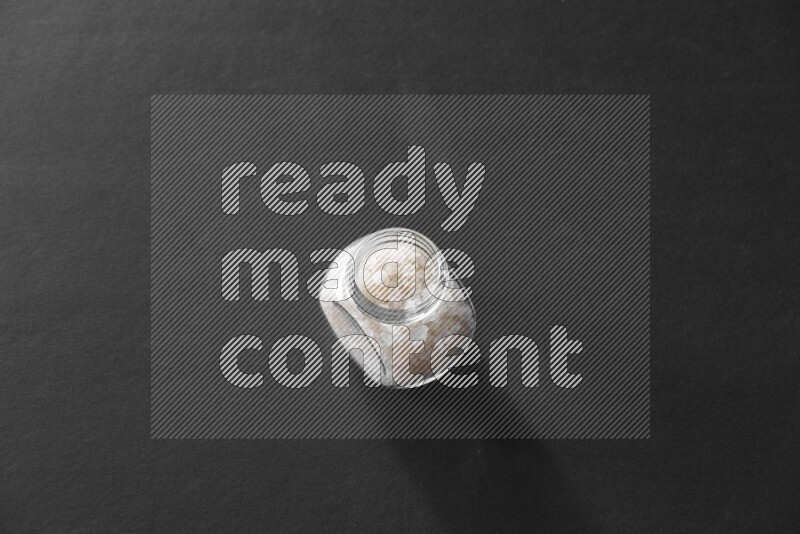 A glass spice jar full of salt on black flooring