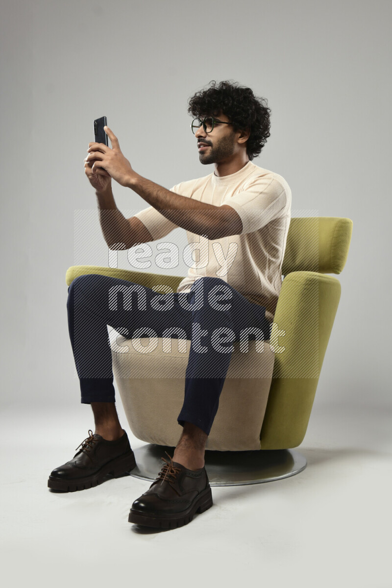 A man wearing casual sitting on a chair shooting with his phone on white background