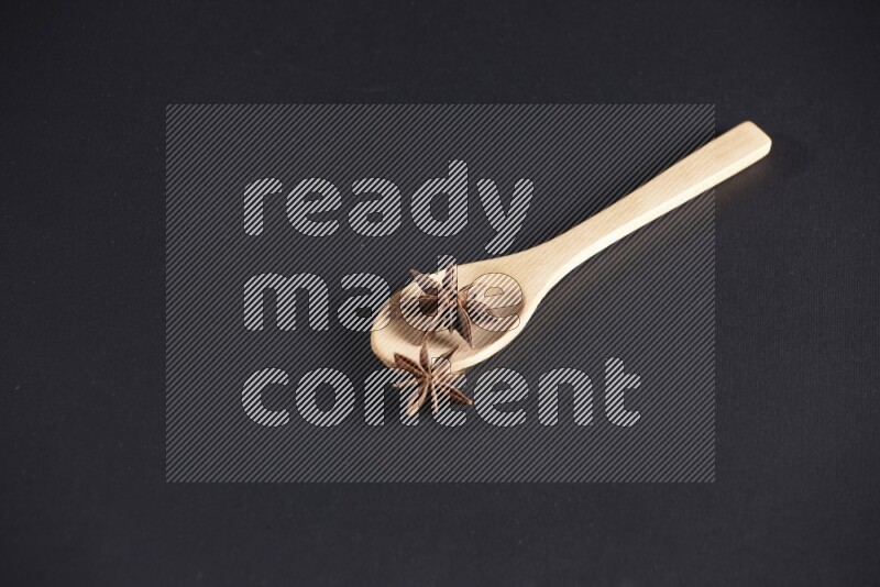 Star Anise in a wooden spoon on more stars anise filling the frame on black flooring
