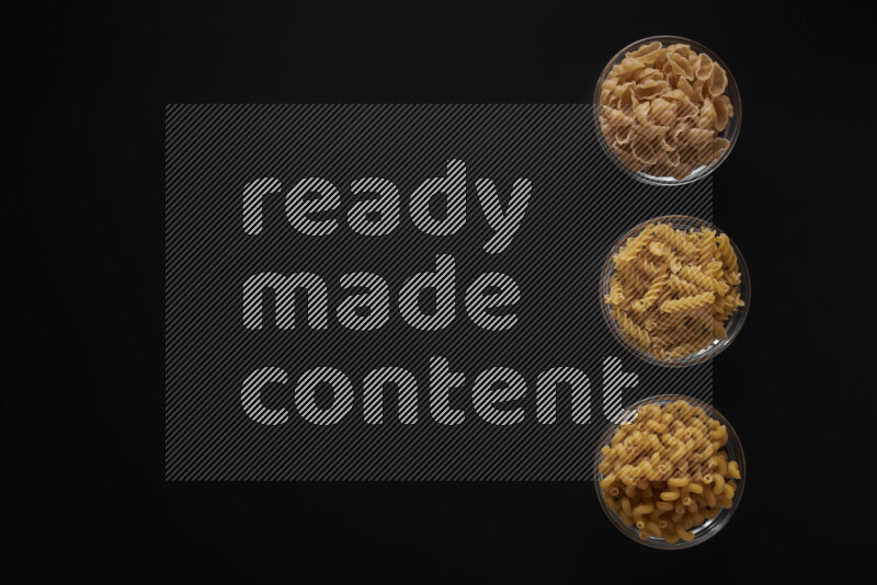 Different pasta types in 3 glass bowls on black background