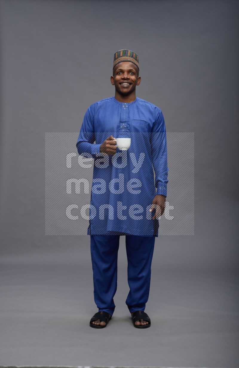 Man wearing Nigerian outfit standing holding mug on gray background