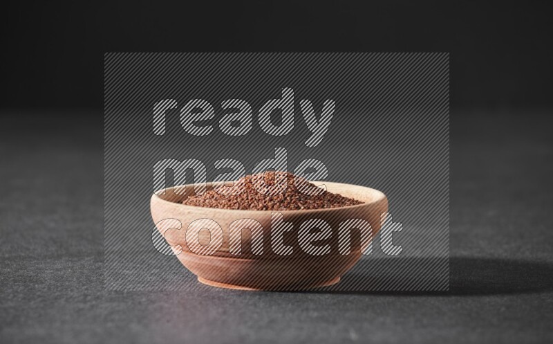 A wooden bowl full of garden cress seeds on a black flooring