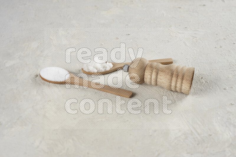2 wooden spoons filled with fine and coarse salt with wooden grinder beside them on white background
