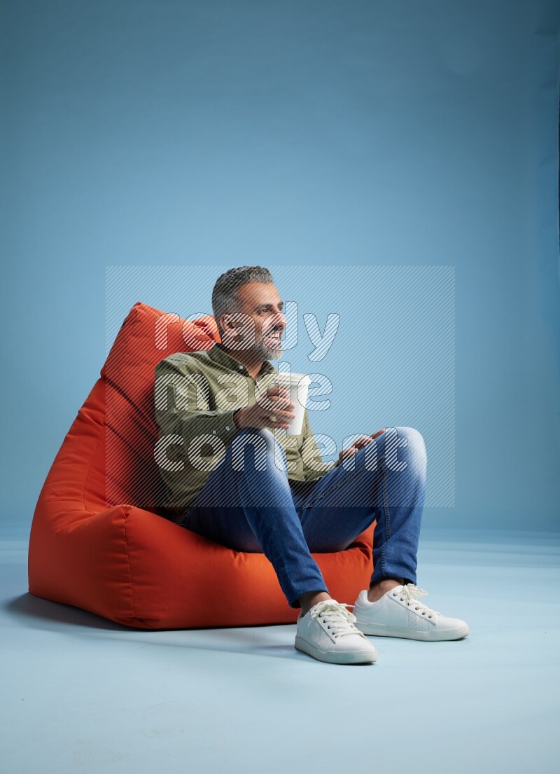 A man sitting on an orange beanbag and drinking coffee