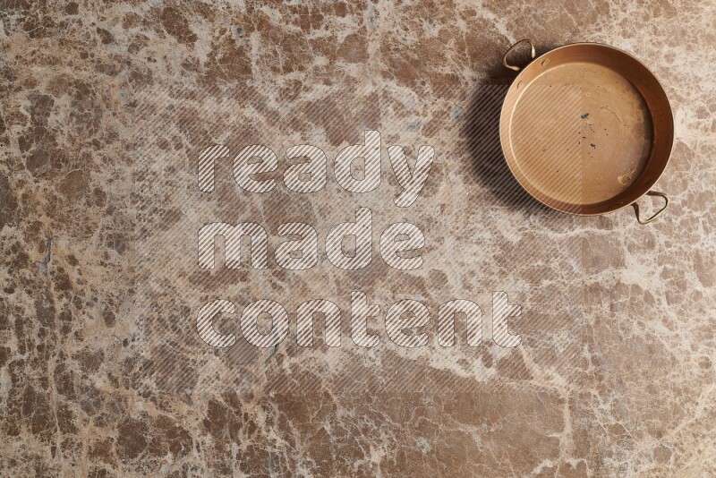 A small copper pan on beige marble background