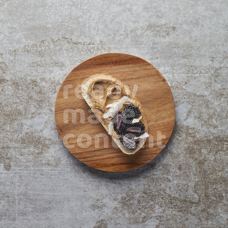 open faced peanut butter sandwich with blackberries  and coconut flakes on a  grey textured background