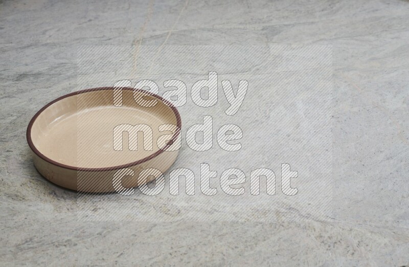 A beige pottery oven bowl on grey marble background