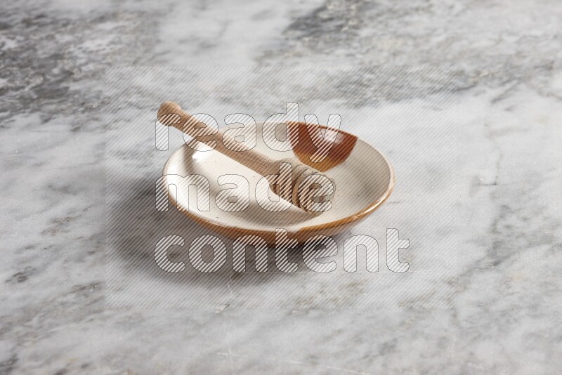 Multicolored pottery plate with wooden honey dipper in it on grey marble background