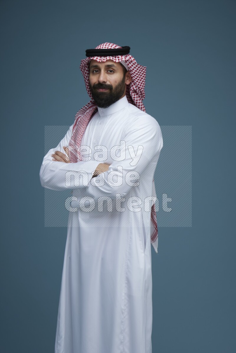 A man posing in a blue background wearing Saudi Thob and Shomag