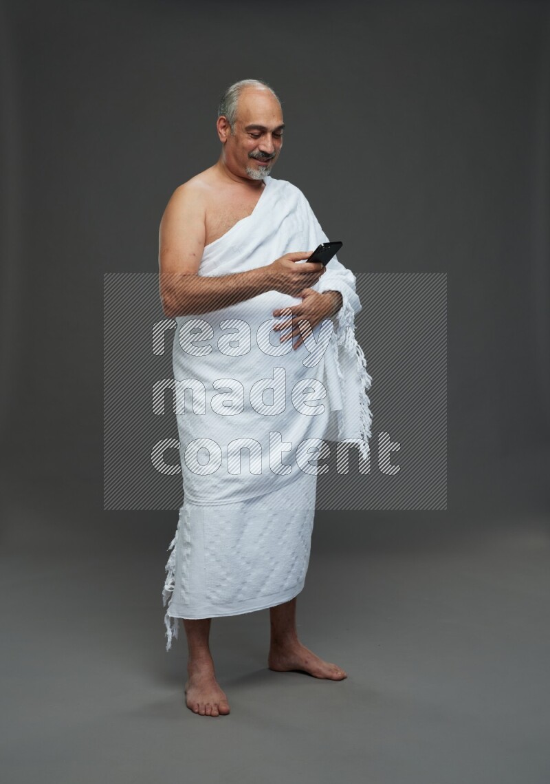 A man wearing Ehram Standing texting on phone on gray background