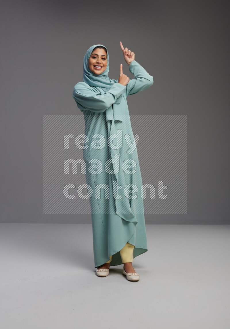 Saudi Woman wearing Abaya standing interacting with the camera on Gray background