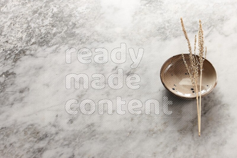 Wheat stalks on multicolored pottery bowl on grey marble background