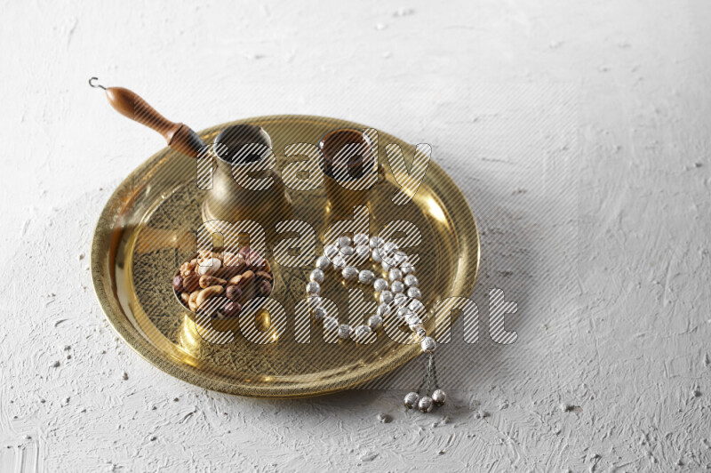 Nuts in a metal bowl with coffee and prayer beads on a tray in a light setup